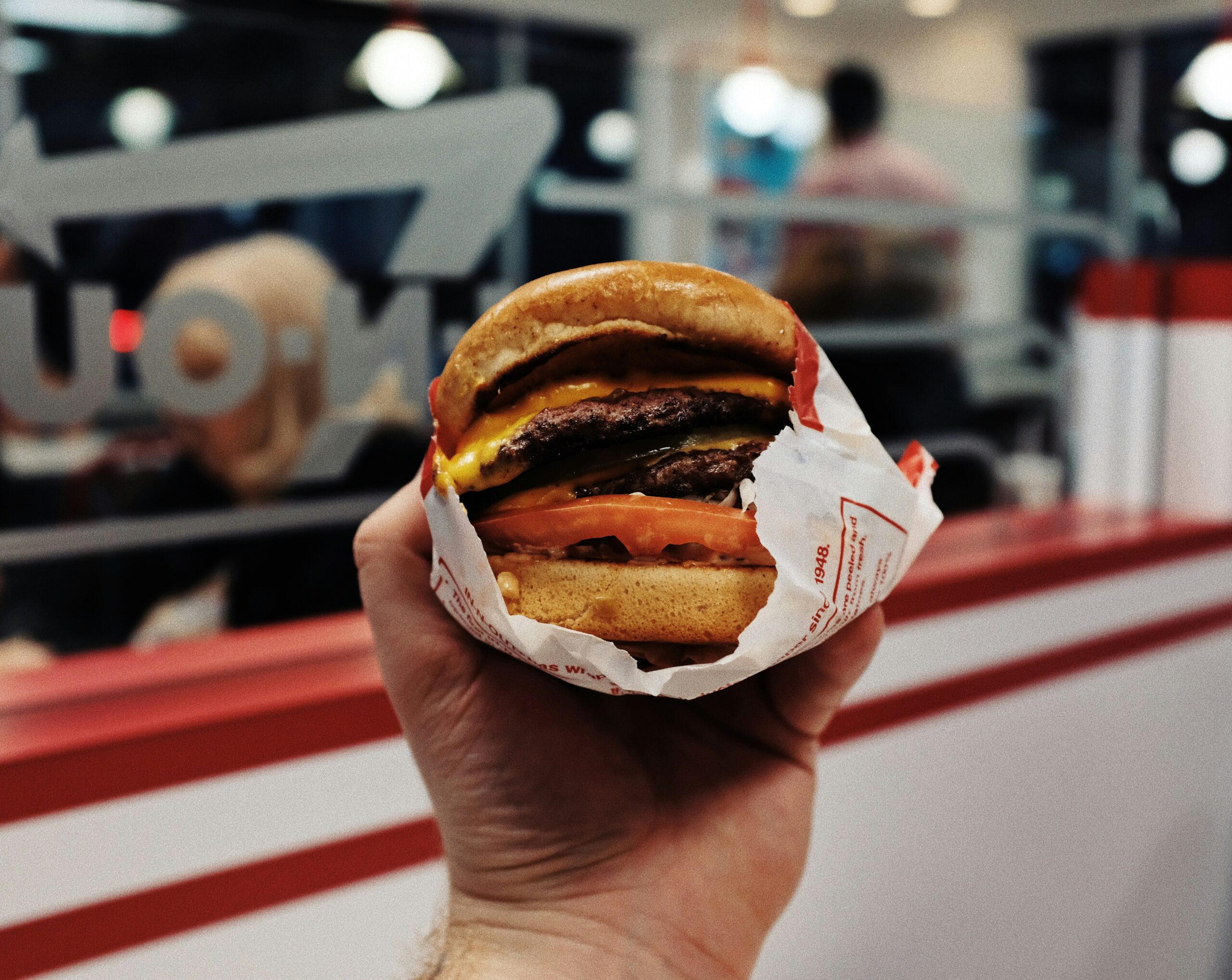 A focused image of a hand holding a burger in the In-N-Out store.